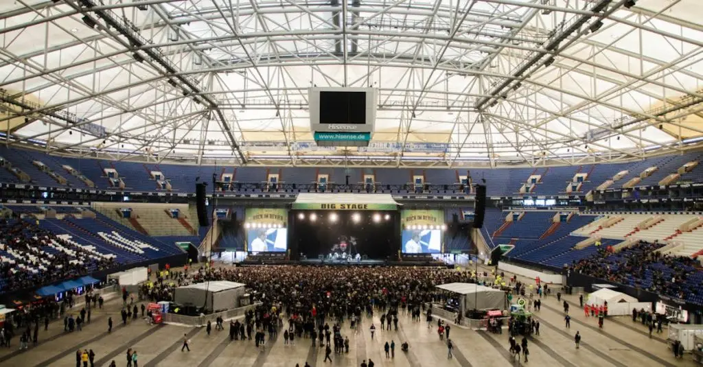 Wide shot of a crowded concert in a large indoor arena with a prominent stage.